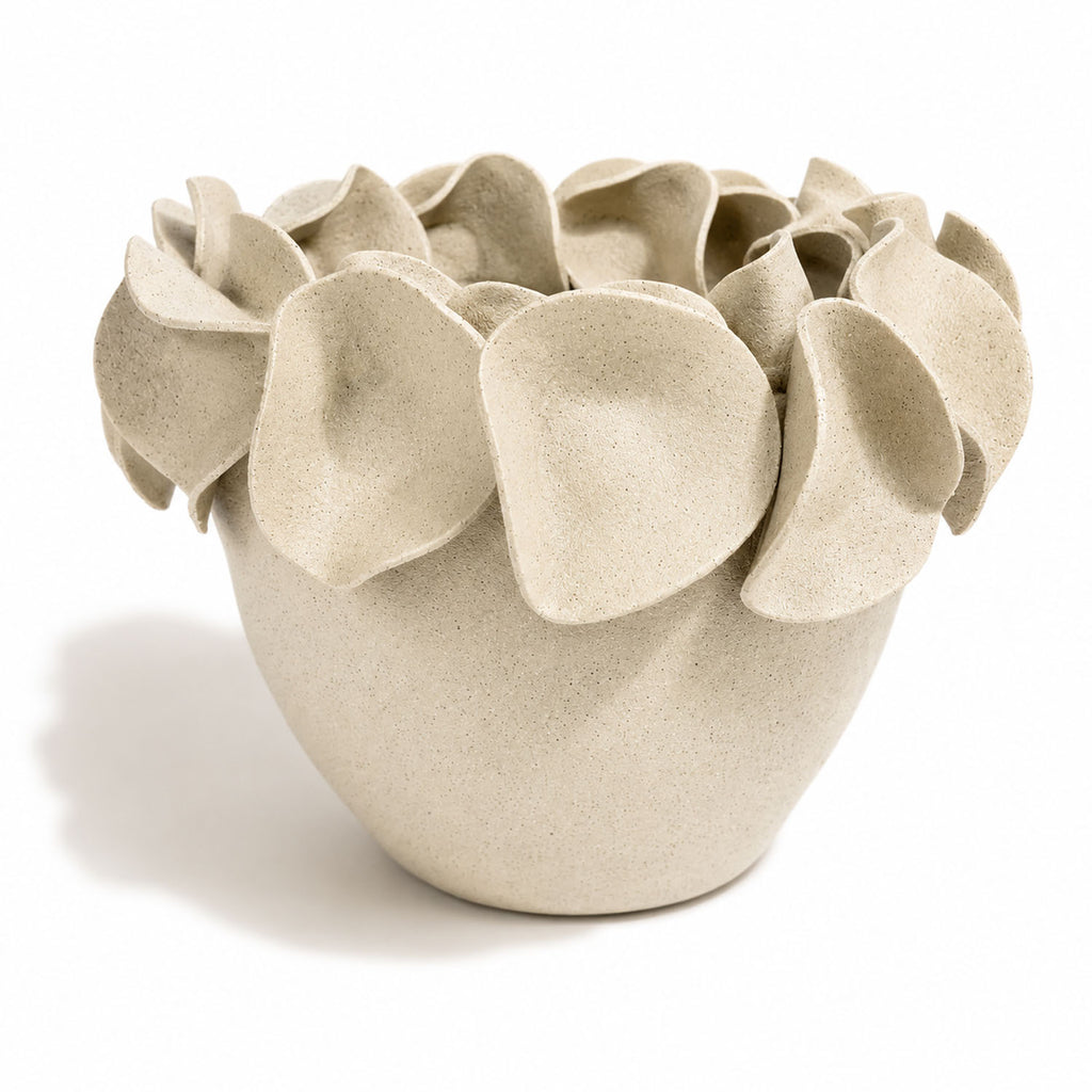 A sculptural ceramic planter with a textured, speckled light beige finish and layered, petal-like protrusions around the rim.