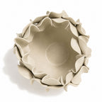 A top-down view of a beige ceramic bowl with a decorative, layered petal-like rim, set against a plain white background with a soft shadow.