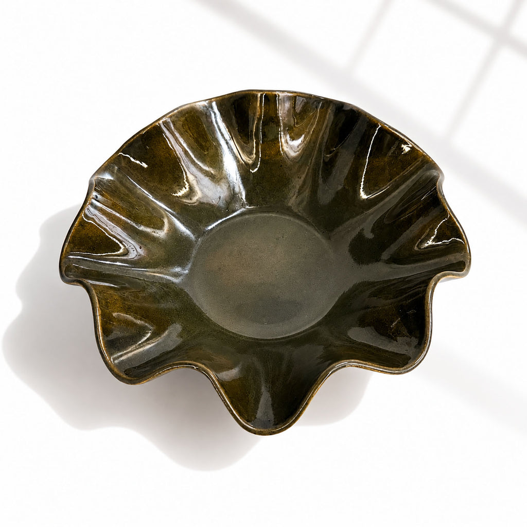 A glossy dark green ceramic bowl with a scalloped, wavy rim, photographed from a top-down angle on a white surface with soft window-light shadows.