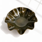 A glossy dark green ceramic bowl with a scalloped, wavy rim, photographed from a top-down angle on a white surface with soft window-light shadows.