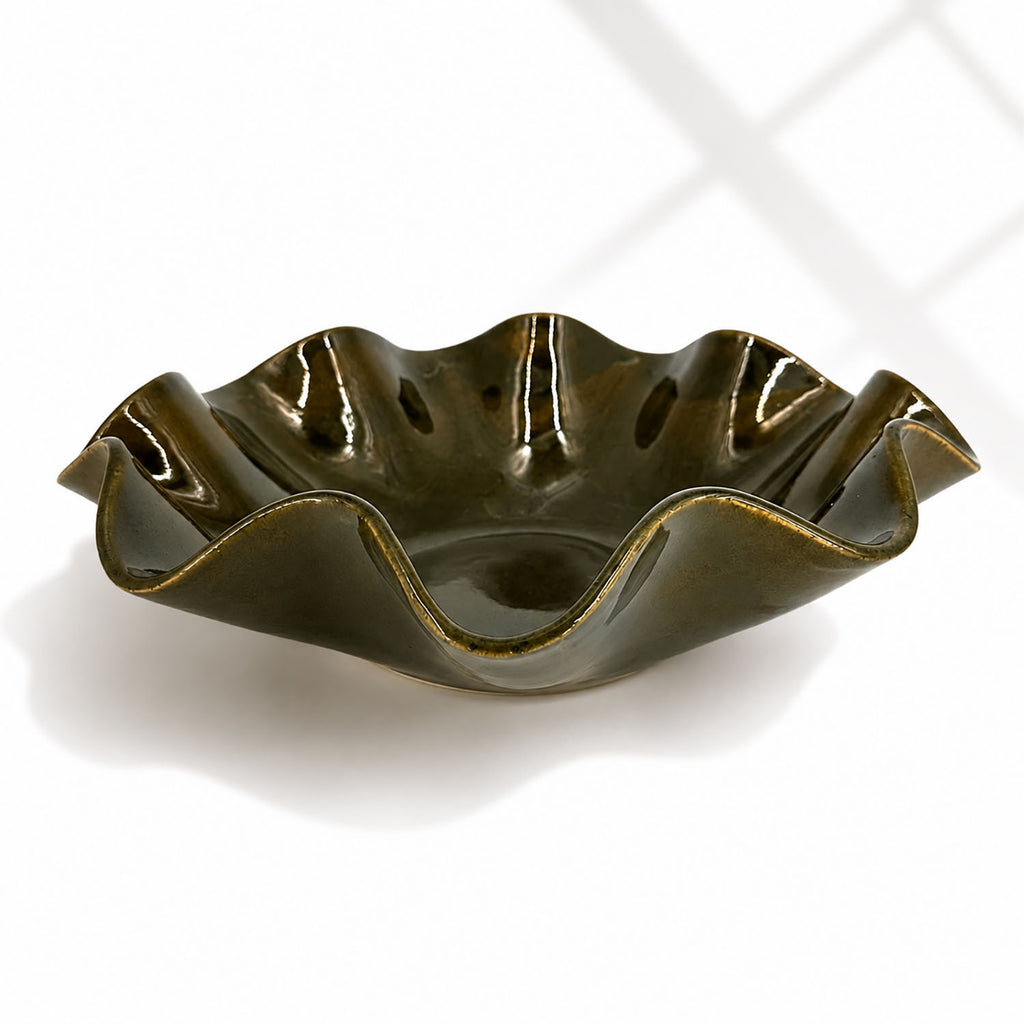 A glossy dark olive green ceramic bowl with a wavy, scalloped rim, shown on a clean white background with soft window shadow patterns.