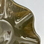 Close-up of a glossy ceramic waved bowl with a scalloped edge and a circular recess, showing a brown and olive glaze on a white background.