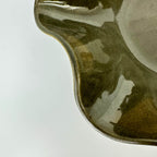 Close-up of a ceramic bowl with a glossy, wavy scalloped rim in a dark olive-brown glaze, set against a plain white background.