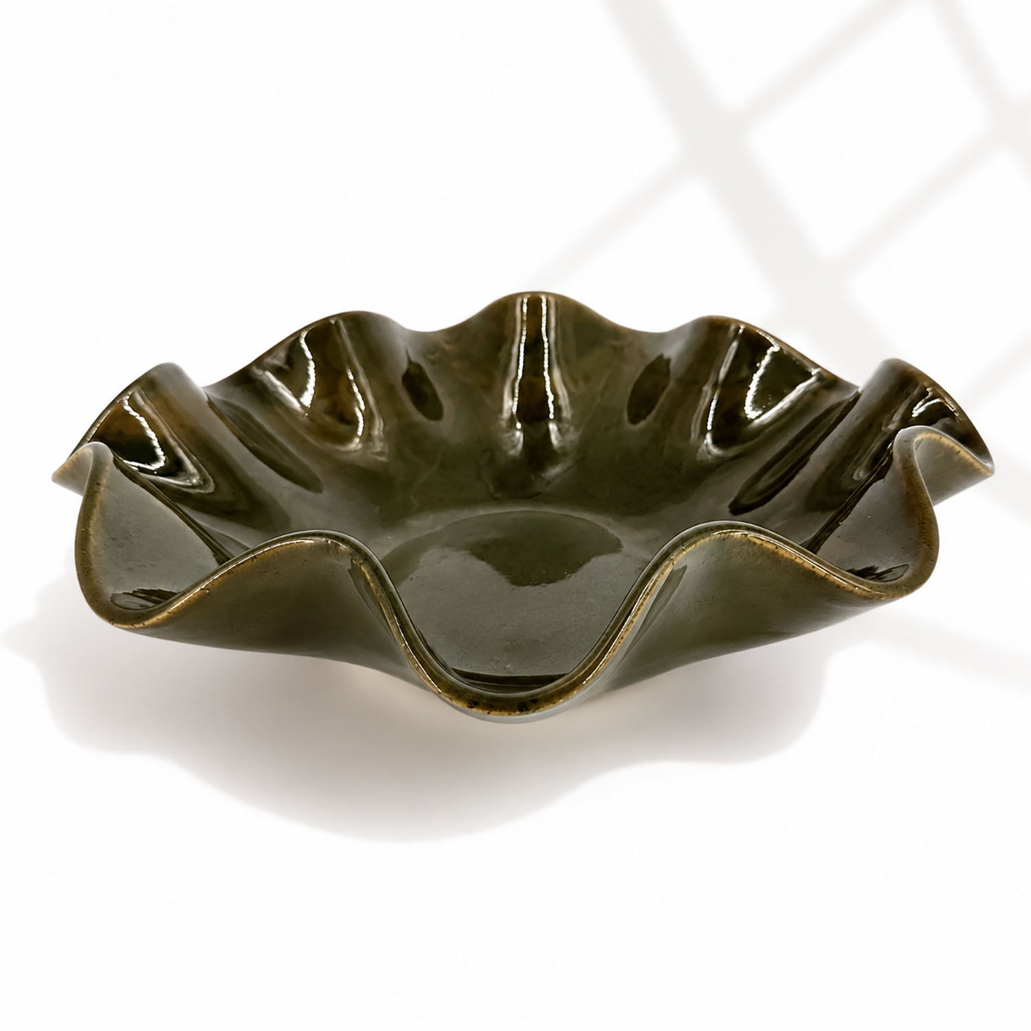A glossy dark olive green ceramic bowl with a wavy, scalloped rim, shown on a white background with soft window shadow patterns.