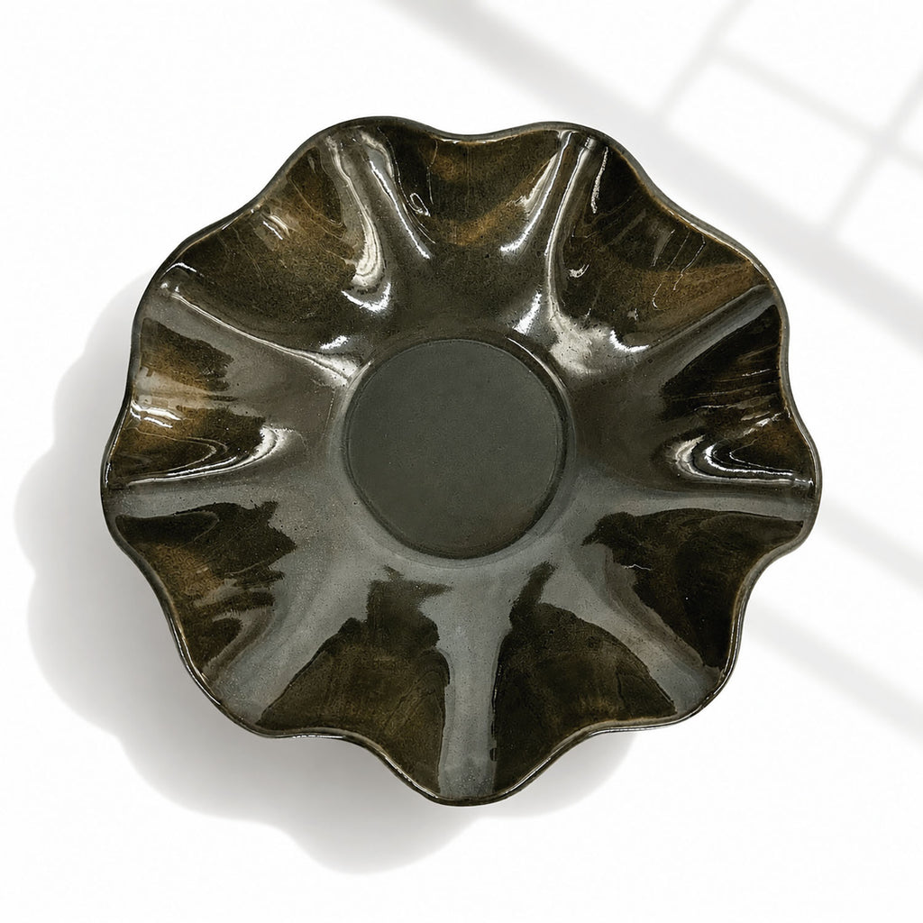 A glossy ceramic bowl with a scalloped, flower-like rim, shown from a top-down perspective on a white surface with soft window shadows.