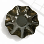 A glossy ceramic bowl with a scalloped, flower-like rim, shown from a top-down perspective on a white surface with soft window shadows.