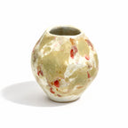A small handmade ceramic vase with a rounded bulbous shape, featuring a mottled glaze of beige, cream, and terracotta red speckles, set against a plain white background.