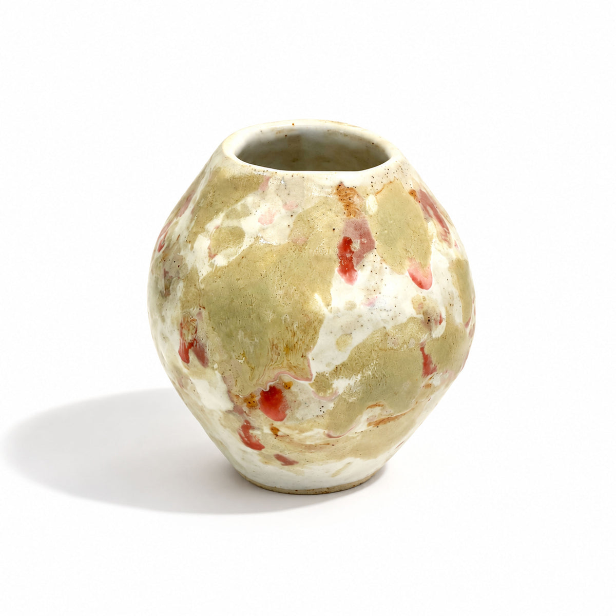 A small handmade ceramic vase with a rounded bulbous shape, featuring a mottled glaze of beige, cream, and terracotta red speckles, set against a plain white background.