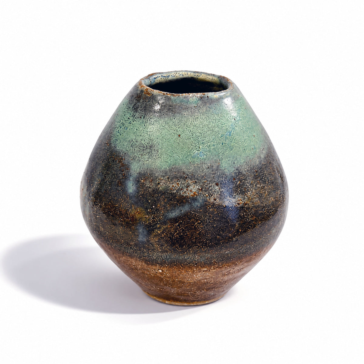 A small handmade ceramic vase with a rounded teardrop shape, featuring a glossy glaze that transitions from a light green at the top to a dark brown and black at the bottom, set against a plain white background.