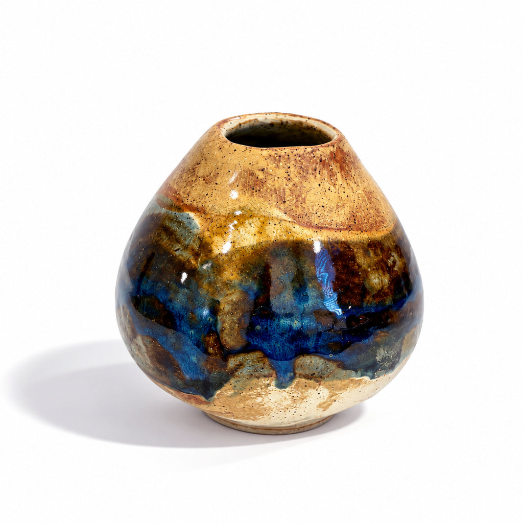 A small handmade ceramic vase with a rounded body and narrow neck, featuring a glossy glaze with a gradient of gold, brown, and deep blue on a white background.