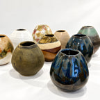 A group of handmade ceramic vases with diverse glazes and earthy tones, arranged on a white surface against a white background.
